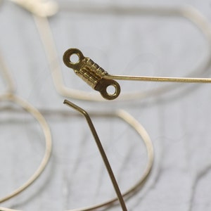May include: A gold-toned metal hinge with two small holes. The hinge is attached to a thin, gold-toned metal wire.