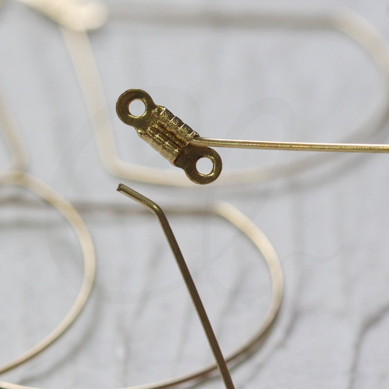 May include: A gold-toned metal hinge with two small holes. The hinge is attached to a thin, gold-toned metal wire.