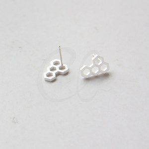 May include: A pair of silver honeycomb stud earrings. The earrings are made of a single piece of metal that is shaped like a honeycomb.