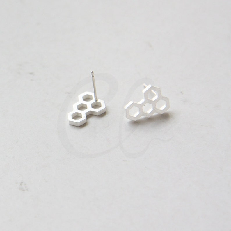 May include: A pair of silver honeycomb stud earrings. The earrings are made of a single piece of metal that is shaped like a honeycomb.