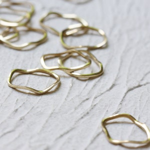 May include: A group of gold-toned, wavy, open rings on a white textured surface.