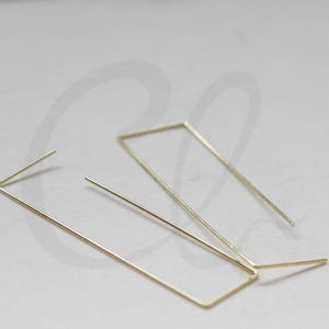 May include: A pair of gold-toned geometric earrings. One earring is a rectangle, the other is a thin, straight line.