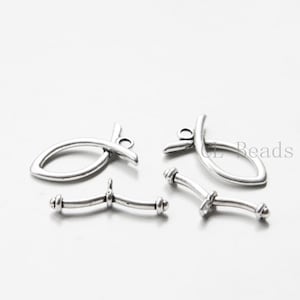 May include: Silver-toned metal fish charms with a loop at the top for attaching to jewellery or other crafts. Two fish charms are shown, along with two curved metal connectors.