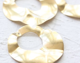 Pode incluir: Três brincos de metal dourado com uma forma irregular ondulada. Os brincos são de tamanhos diferentes e têm um furo na parte superior para pendurar.
