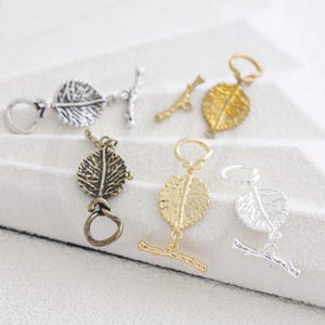 May include: Assortment of leaf-shaped toggle clasps in various metallic finishes, including silver, gold, and bronze. Each clasp features a detailed leaf design and a coordinating bar or ring closure. Ideal for jewelry making.