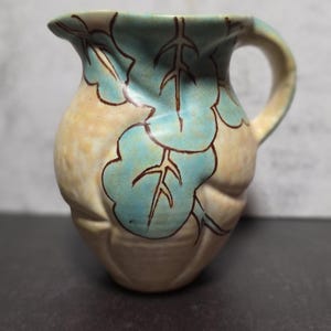 May include: A white ceramic mug with a black handle and the text "But First, Coffee" in a black, handwritten-style font. The mug is on a white surface.