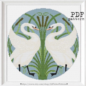 Pode incluir: Um padrão de ponto de cruz emoldurado com dois cisnes brancos voltados um para o outro, cercados por juncos verdes e taboas em um fundo azul claro. As palavras "PDF pattern" estão no canto superior direito.