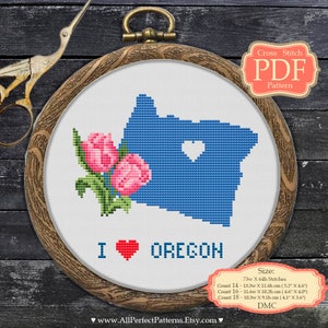 May include: A cross stitch pattern PDF for a blue outline of the state of Oregon with a red heart in the center and a bouquet of pink roses in the lower left corner. The text "I ♥ OREGON" is below the outline. The pattern is available in four sizes: 14, 16, 18, and 20 count.