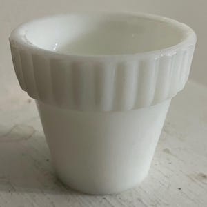 May include: A small, white, vintage-style planter or container. The container has a cylindrical shape with a flared top and a ribbed design around the rim. The surface is smooth and glossy, with a clean, minimalist aesthetic.