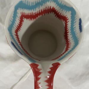 May include: White ceramic pitcher with a red and blue zigzag pattern around the rim and on the handle. The interior is plain. The pitcher is designed for serving beverages.