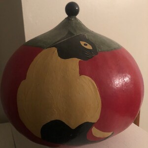 May include: A ceramic gourd-shaped jar with a black knob on top. The jar is painted red with a black and tan cat design.