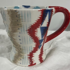 May include: A white ceramic mug with a black handle and the text "But First, Coffee" in a bold, black font. The mug is set against a neutral background, highlighting its simple design.