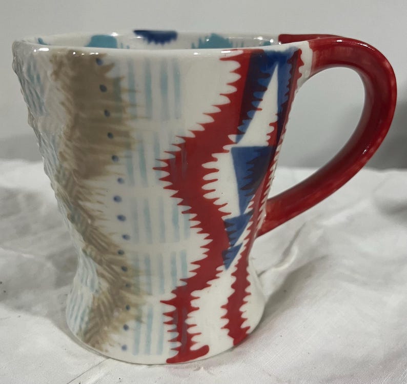 May include: A white ceramic mug with a black handle and the text "But First, Coffee" in a bold, black font. The mug is set against a neutral background, highlighting its simple design.