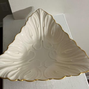 May include: A white ceramic triangular dish with a gold rim and a decorative floral design.