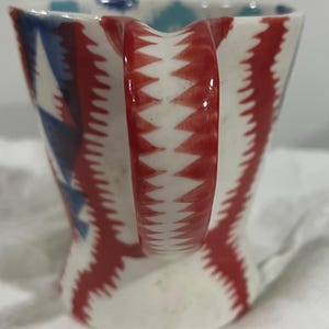 May include: A white ceramic mug with a black handle and the text "But First, Coffee" in a bold, black font. The mug is filled with a dark liquid, likely coffee, and sits on a light-colored surface.