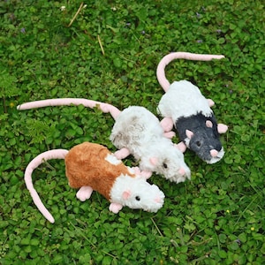 May include: Three plush rat toys with soft fur in brown and white, light gray and white, and dark gray and white. Each toy features a long pink tail, small pink ears, and a pink nose, designed with a realistic shape and textured fabric finish.