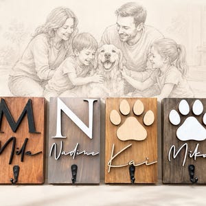 May include: Four rectangular wooden wall hooks featuring raised letters and paw print cutouts. Each plaque displays a name in script font and a single black metal hook at the bottom. The designs include the names Mila, Nadine, Kai, and Mika.