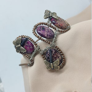 May include: A copper wire wrapped bracelet featuring purple and brown jasper stones and gold butterfly charms.