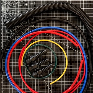 May include: An assortment of electrical components, including black corrugated tubing, red, blue, yellow, and green flexible tubing, and black connectors. The items are arranged on a black grid surface.