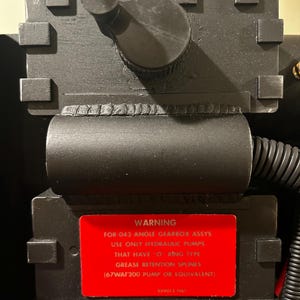 Puede incluir: Primer plano de una etiqueta de advertencia negra en una caja de metal negra. La etiqueta dice: "ADVERTENCIA PARA-043 ÁNGULO DE CAJA DE CAMBIOS ASSYS UTILICE SOLO BOMBAS HIDRÁULICAS QUE TENGAN TIPO DE ANILLO DE RETENCIÓN DE GRASA (BOMBA 67WAF200 O EQUIVALENTE) 559013 1167"