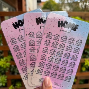 May include: Three rectangular cards with a pink and blue gradient background are held in a hand. Each card has the words "HOME fund" in black script at the top. Below the text are rows of small house illustrations.