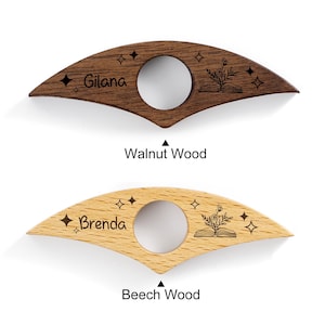 May include: Two wooden thumb page holders. One is dark brown walnut wood with the name "Gilana" and the other is light brown beech wood with the name "Brenda". Both have a circular opening and star and book designs.