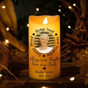 Könnte beinhalten: Eine gelbe LED-Kerze mit einem Foto einer Frau in einem kreisförmigen Rahmen. Die Kerze trägt den Text "Always Loved, Forever Missed, Never Forgotten" und "Always in our Thoughts Forever in our Hearts". Der Name "Elodie Taylor" und die Daten "1950-2023" sind ebenfalls aufgedruckt.
