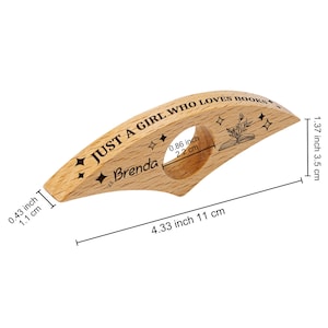May include: A wooden book page holder with the text "JUST A GIRL WHO LOVES BOOKS" and the name "Brenda". The holder is 4.33 inches (11 cm) long and features a circular opening. It has a decorative design of stars and a book.