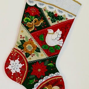 May include: A handmade Christmas stocking with a patchwork design. The stocking features red, green, and cream-colored panels adorned with embroidered flowers, a white dove, and gold sequin accents. The top is white with gold trim.