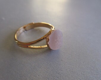May include: A gold ring with a delicate split band and a pink, textured stone.