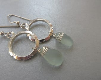 May include: A pair of silver earrings with a circular design and a teardrop-shaped piece of light blue glass hanging from each.