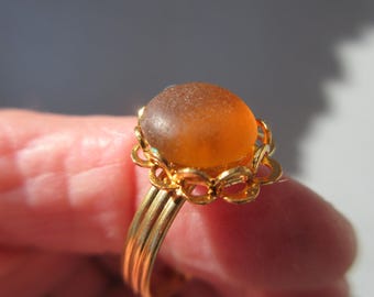 May include: A gold ring with a large, oval-shaped amber glass stone set in a decorative, floral-shaped setting.