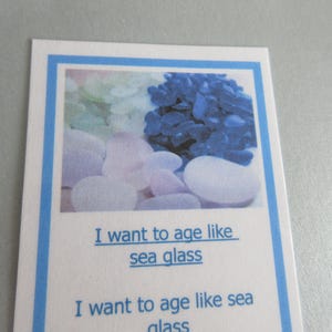 May include: A white card with a blue border features an image of sea glass and the text "I want to age like sea glass." The image shows smooth, rounded stones in shades of white, blue, and pink.