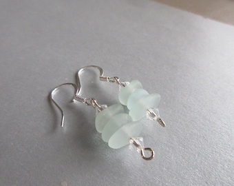 May include: A pair of silver earrings with light blue sea glass beads. The earrings are made with a simple wire design and have a delicate look.