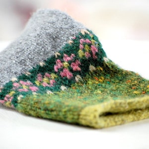 Puede incluir: Gorro de punto doblado con la parte superior gris y la inferior verde y amarilla. Una banda verde con flores rosas y amarillas separa las dos secciones. El gorro está hecho de un hilo texturizado.