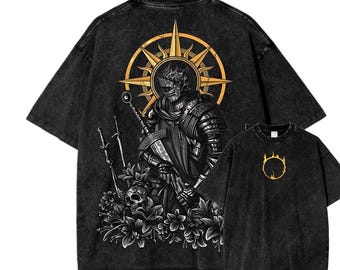 May include: Two black graphic t-shirts. The larger shirt features a detailed illustration of a knight with a sword, surrounded by flowers and a skull, set against a golden sunburst. The smaller shirt displays a golden emblem. Both shirts have a vintage wash.