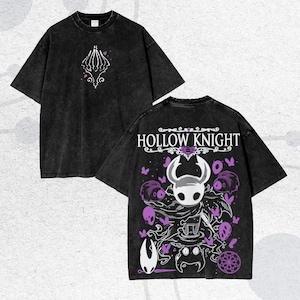 May include: Two black t-shirts with a faded, vintage look. One shirt features a white and purple design on the front, while the other displays the words "HOLLOW KNIGHT" and a character graphic on the back. The shirts have short sleeves.