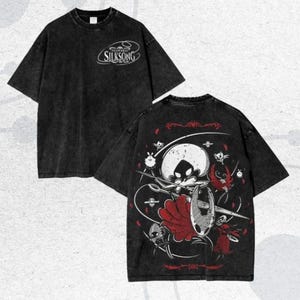May include: Black t-shirt with the word "Silksong" in white on the front. The back of the shirt features a graphic of a character with a red cape, a shield, and a needle. The design is in white and red.
