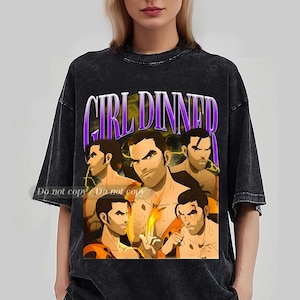 May include: Black t-shirt with a graphic featuring the text "GIRL DINNER" in purple and white, with an illustration of several muscular men. The design has a vintage, distressed look.