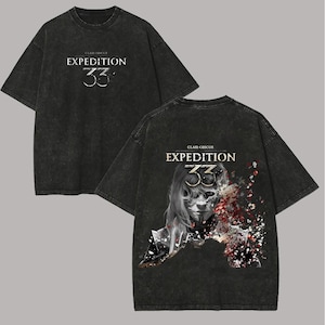 Puede incluir: Camiseta gris oscuro con el texto "CLAIR OBSCUR EXPEDITION 33" en la parte delantera. La parte trasera de la camiseta presenta un gráfico de una persona con rostro de calavera y elementos florales.