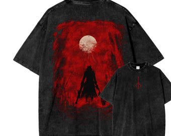 May include: Two black t-shirts. The larger shirt features a red background with a silhouetted figure and a white moon. The smaller shirt has a red symbol on the chest. Both shirts have a faded, vintage look.