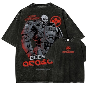 以下が含まれることがあります： 黒のアシッドウォッシュTシャツ。未来的なサイボーグのグラフィック、赤色の「Adam Smasher」と「Body Arasaka Cyberpunk」の文字が特徴です。小さいTシャツには、赤色のArasakaのロゴと文字が表示されています。