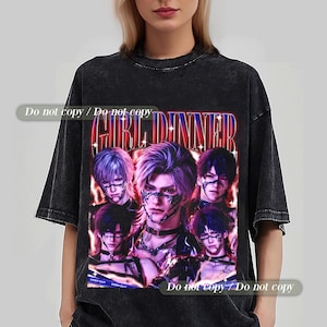 Può includere: T-shirt nero oversize con una grafica di cinque figure stilizzate con capelli viola e neri e disegni sul viso. Il testo "GIRL DINNER" è visualizzato in un font retrò. La maglietta ha un aspetto vintage.