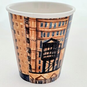 Puede incluir: Un vaso de caf&eacute; de papel con borde blanco, decorado con una ilustraci&oacute;n detallada de una fachada de edificio. El dise&ntilde;o presenta tonos marrones, azules y negros, con elementos arquitect&oacute;nicos, dando un aire vintage.