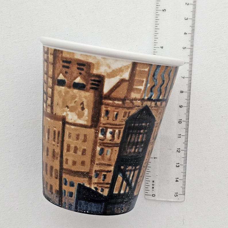 Puede incluir: Una taza de cer&aacute;mica con un dise&ntilde;o de paisaje urbano. La taza tiene un borde blanco y una forma c&oacute;nica. La obra de arte representa edificios en tonos marrones, beige y azules. La taza mide aproximadamente 10 cm de altura.