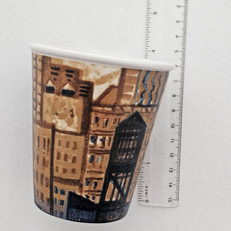 Puede incluir: Una taza de cer&aacute;mica con un dise&ntilde;o de paisaje urbano. La taza tiene un borde blanco y una forma c&oacute;nica. La obra de arte representa edificios marrones y azules. La taza mide aproximadamente 13 cm de altura.