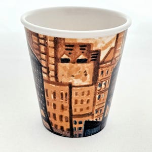 Puede incluir: Una taza de cer&aacute;mica blanca con un asa negra y el texto "But First, Coffee" en negrita negra. La taza se encuentra sobre un fondo borroso, sugiriendo un ambiente acogedor.