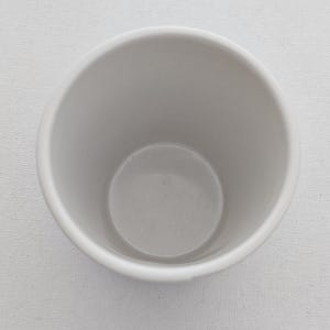 Puede incluir: Una taza de cer&aacute;mica blanca con forma redondeada. La taza tiene un acabado liso y mate y una amplia abertura. El interior de la taza es de color gris claro. La taza est&aacute; vac&iacute;a y parece limpia.
