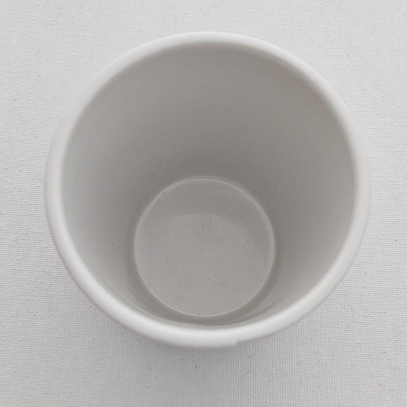 Puede incluir: Una taza de cer&aacute;mica blanca con forma redondeada. La taza tiene un acabado liso y mate y una amplia abertura. El interior de la taza es de color gris claro. La taza est&aacute; vac&iacute;a y parece limpia.