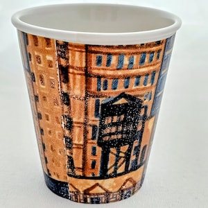 Puede incluir: Una taza de caf&eacute; de papel desechable con un borde blanco y un dise&ntilde;o arquitect&oacute;nico marr&oacute;n y azul. La taza presenta un patr&oacute;n repetitivo de edificios y estructuras.